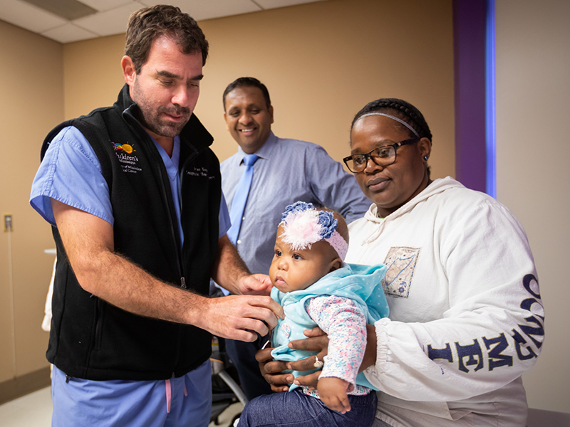 Cindy Thompson holds Gabbi Smith, heart transplant patient, while Dr. Brian Kogon checks her month after surgery. Looking on is Dr. Avichal Aggarwal, pediatric cardiologist.